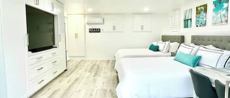 A modern bedroom with two beds, a desk, and a television.
