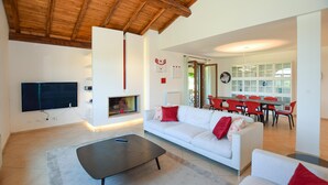 Un salon moderne doté d’une cheminée, d’un téléviseur à écran plat et d’un coin repas avec des chaises rouges.