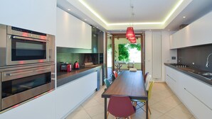 Une cuisine moderne dotée d’appareils électroménagers intégrés, un coin repas avec une longue table et des chaises, et une vue sur la verdure environnante.