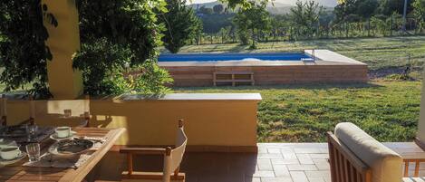 An outdoor patio with a wooden table and chairs, a small pool, and a view of a hilly landscape.