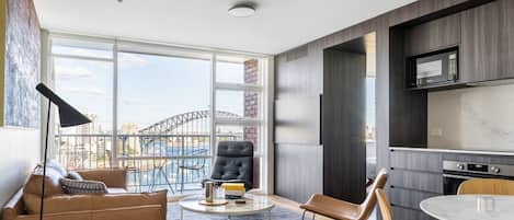 Uma sala de estar moderna com vista para a Ponte Sydney, uma área de jantar com mesa redonda e uma cozinha com micro-ondas embutido.