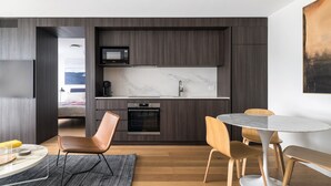 Una cocina moderna con armarios de madera oscura, encimera blanca y microondas integrado. Hay una zona de comedor con una mesa redonda y sillas de madera.
