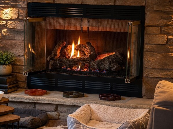 Una chimenea con leña, un muro de piedra y una zona de estar acogedora con cojines.