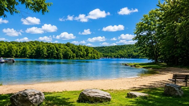 Vista de un lago con playa de arena, rocas grandes y un banco.