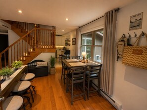 Ein gemütliches Interieur mit einer Holztreppe, einem Essbereich mit Tisch und Stühlen sowie einer Küche im Hintergrund.