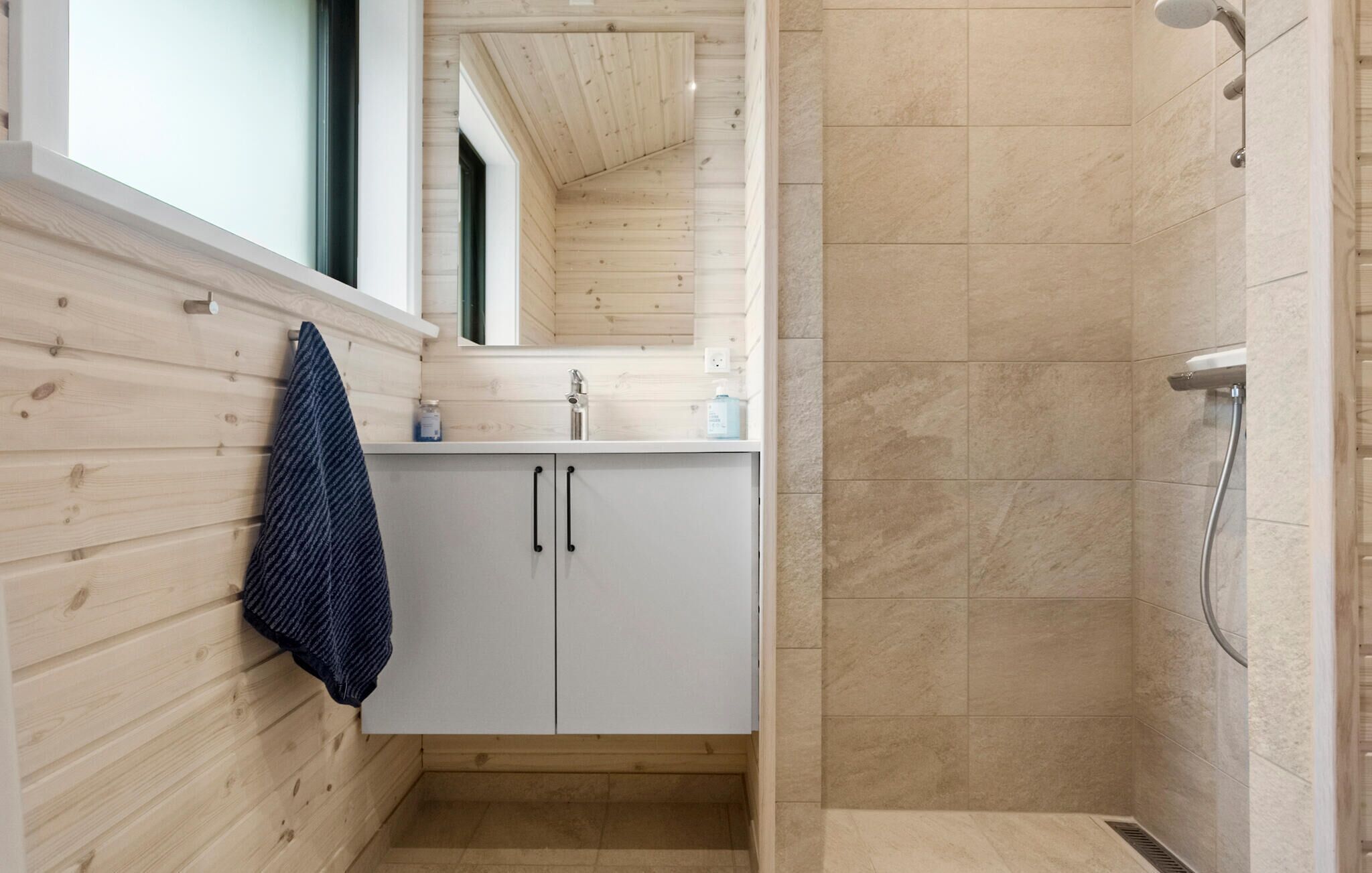 Un baño con paredes de madera, un lavamanos blanco y una zona de ducha.