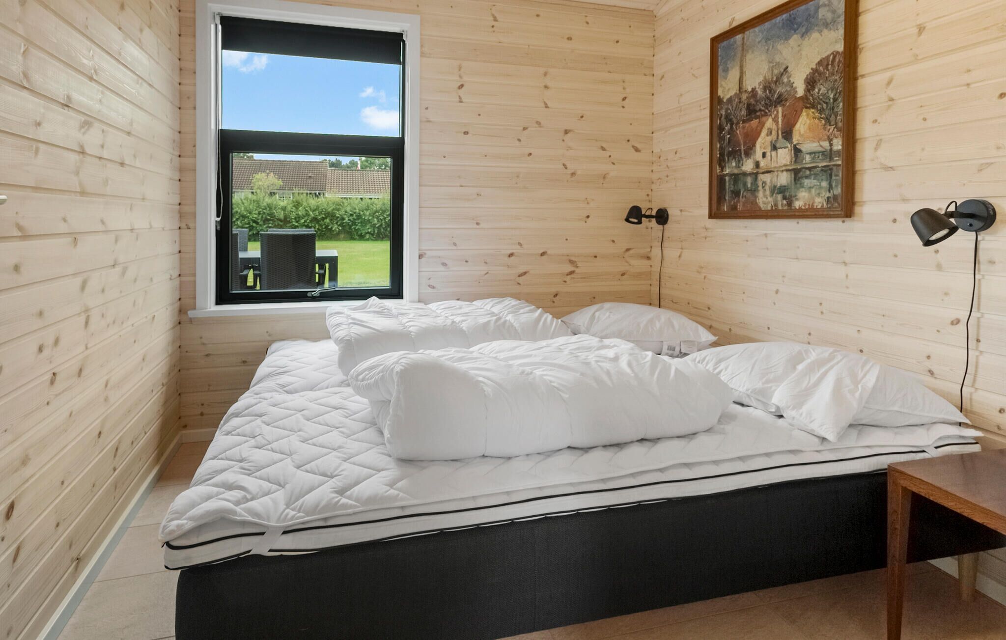A bedroom with a bed, a window, a painting, and a desk.