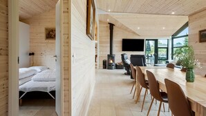 Un interior moderno con techo de madera, chimenea, zona de comedor con sillas y cama con ropa de cama blanca.