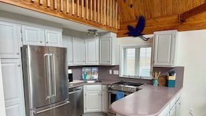 Una cocina moderna con armarios blancos, electrodomésticos de acero inoxidable, techo de madera y una ventana con persianas.