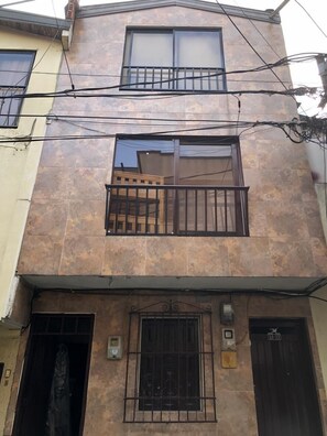A multi-story building with a tiled facade, two balconies with metal railings, and a door with a security keypad.