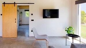 A modern living room with a sliding door, a mounted TV, a grey chair, and a small table with a plant. - Apartamentos aronces  (Cudillero)