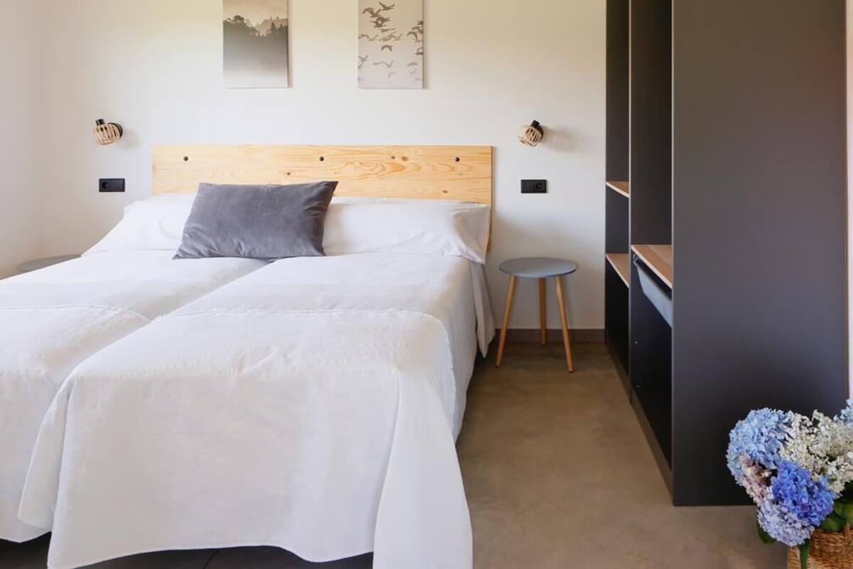 Quarto com uma cama de casal, duas luminárias fixadas na parede, uma pequena mesa redonda e um guarda-roupa escuro.