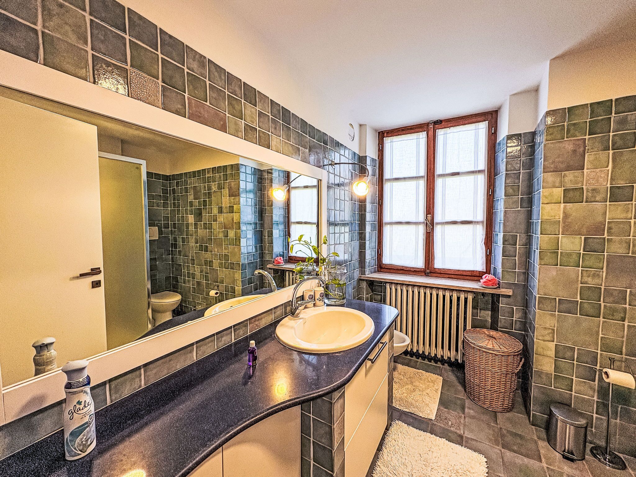 A bathroom with a large mirror, a sink, a window, and a radiator.