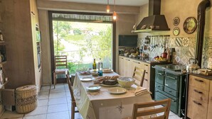 A dining area with a table set for four, a kitchen with a stove and various utensils, and a view of greenery outside. - Del Respiro by Interhome (Asti)