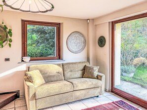 A beige sofa with cushions, a window with a view of greenery, a decorative plate, and a patterned rug.