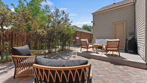 A patio area with wicker furniture, a brick floor, and a view of a house.