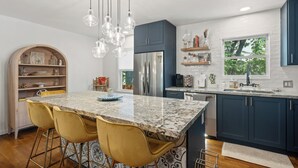 A modern kitchen with a marble island, stainless steel appliances, and yellow bar stools.