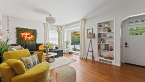 A modern living room with a yellow armchair, a round ottoman, a neon sign, and a bookshelf.
