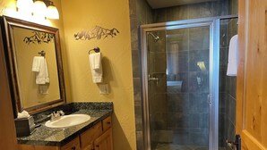Een badkamer met een wastafel met granieten blad, houten kastjes, een grote spiegel en een douche met glazen wanden.