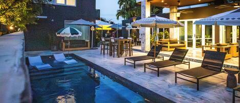 Un área junto a la piscina con sillones de descanso, sombrillas y mobiliario para comer.