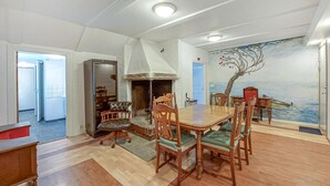 Een eethoek met een houten tafel en stoelen, een open haard en een muurschildering van een boom aan zee.