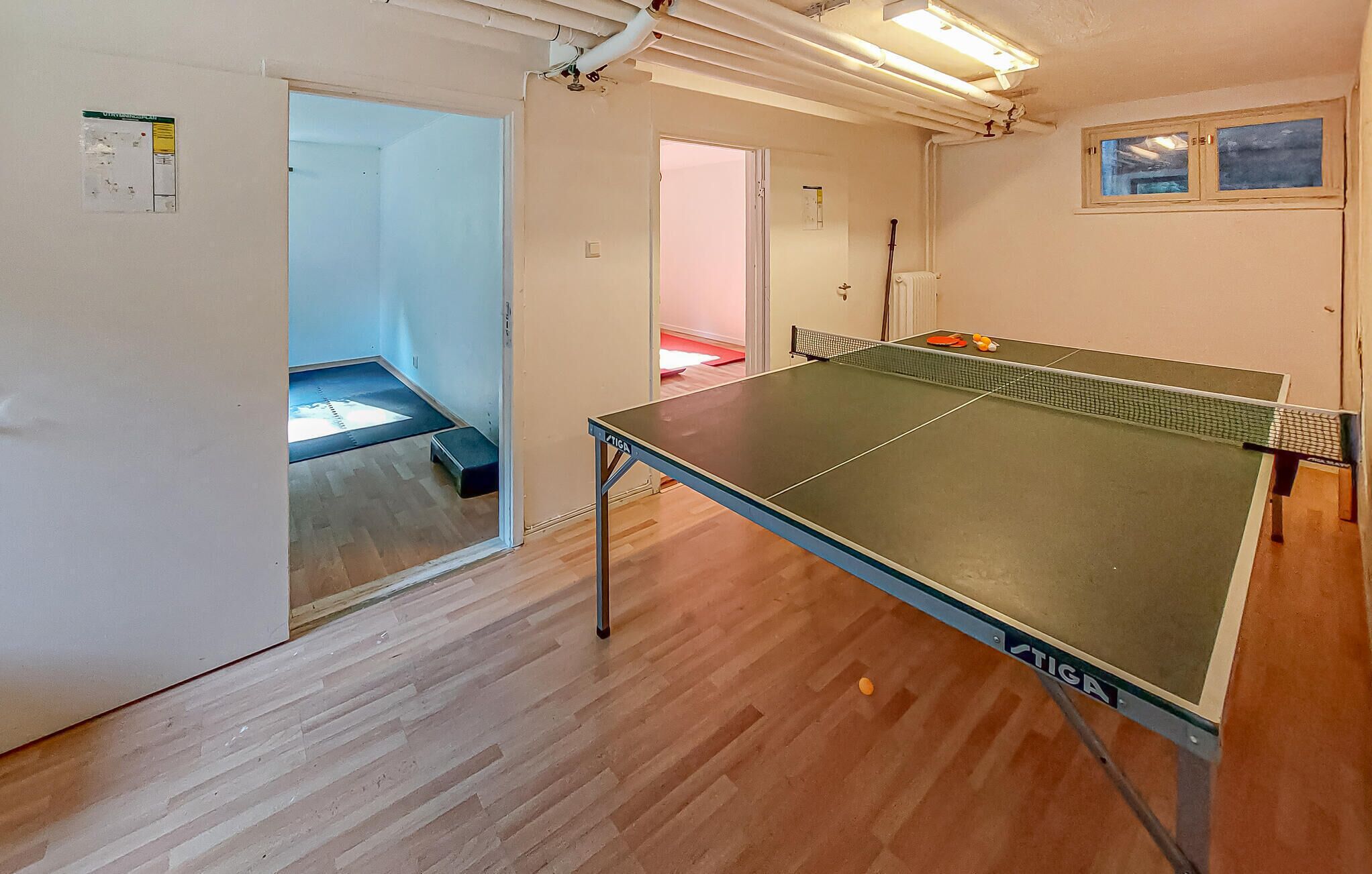 Une pièce avec une table de ping-pong, un plancher en bois et une porte donnant sur une autre pièce.