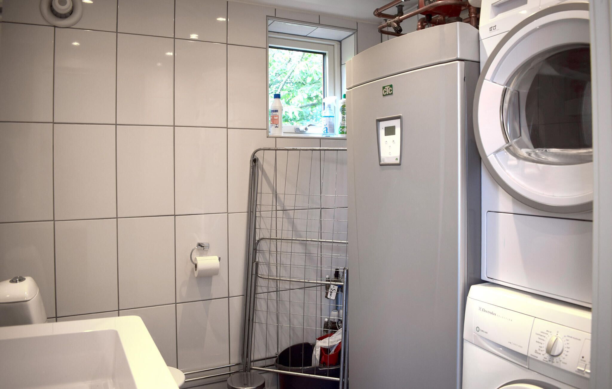 A compact bathroom with a washing machine, a toilet, and a shower area with a metal rack.