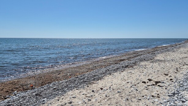 En strand med en stenet kystlinje og roligt hav under en klar himmel.