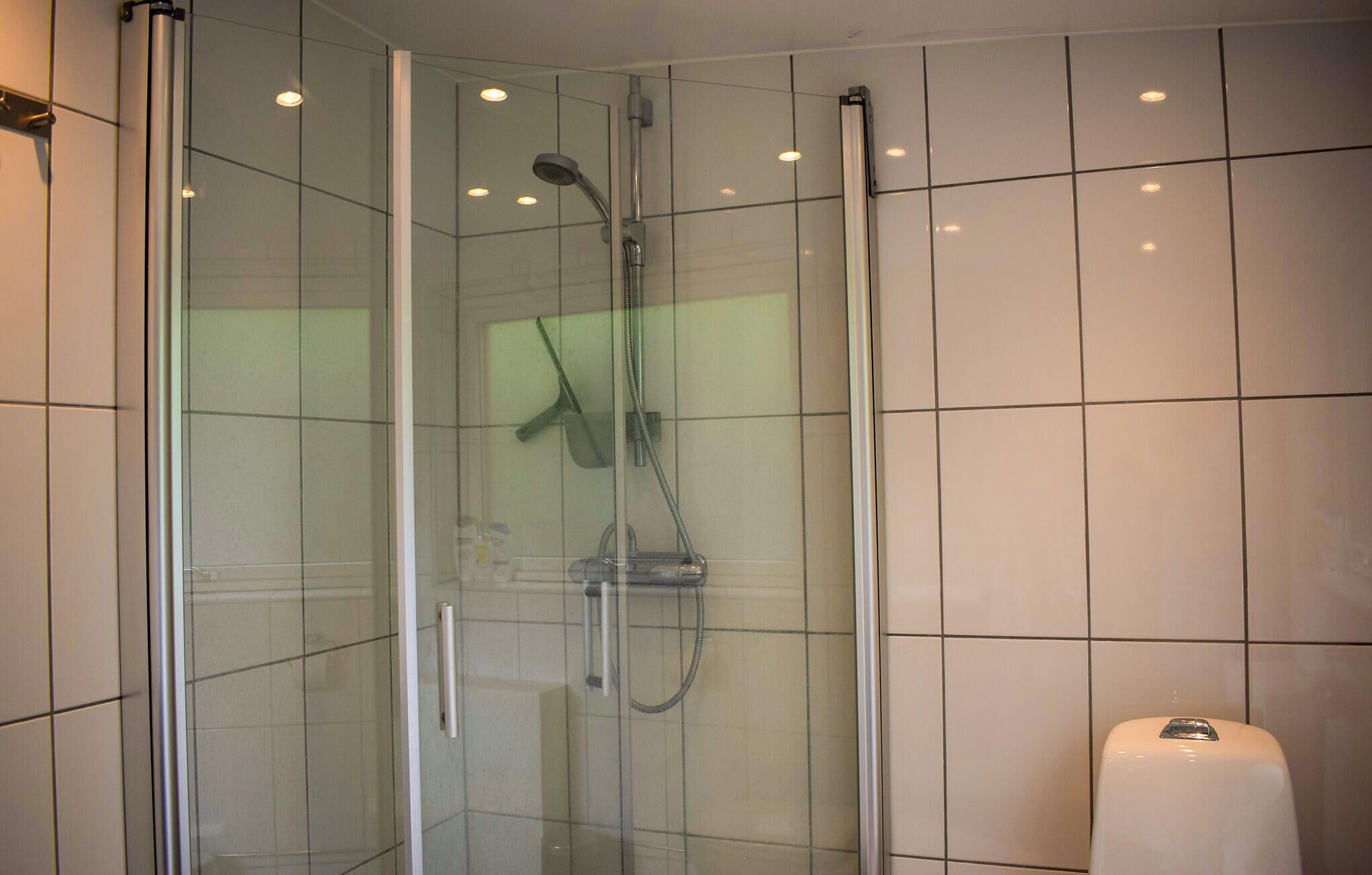 A glass-enclosed shower with a handheld showerhead and a handheld shower attachment.