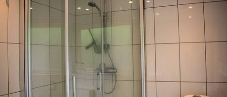 A glass-enclosed shower with a handheld showerhead and a handheld shower attachment.