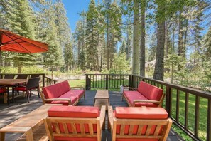 A deck with wooden furniture and red cushions, surrounded by tall trees.
