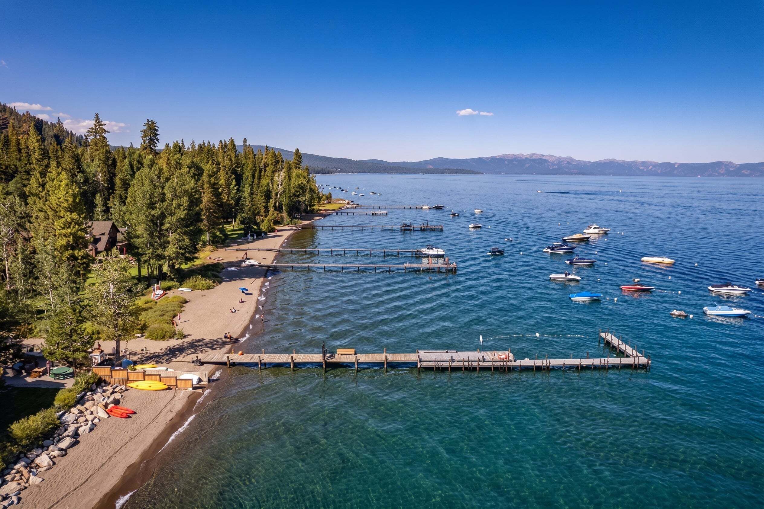 A lakeside beach with clear water, boats, and a dock.