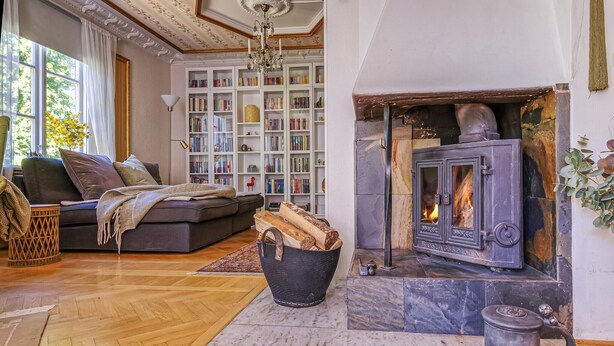 A cozy living room with a fireplace, a sofa, a bookshelf, and a large window.