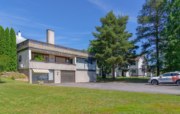 A modern two-story house with a garage, surrounded by a grassy lawn and tall trees.