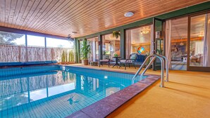 A pool area with a wooden ceiling, a glass-tiled pool, and outdoor seating with chairs and tables.