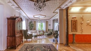 A spacious living room with a large wooden cabinet, a green sofa, a chandelier, and a patterned rug.