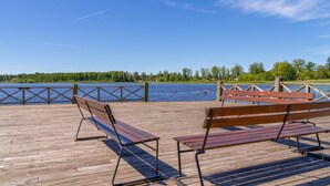 A wooden pier with benches overlooking a calm lake, surrounded by trees and a clear sky.