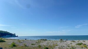 Uma praia rochosa com vegetação rasteira e um céu azul límpido.