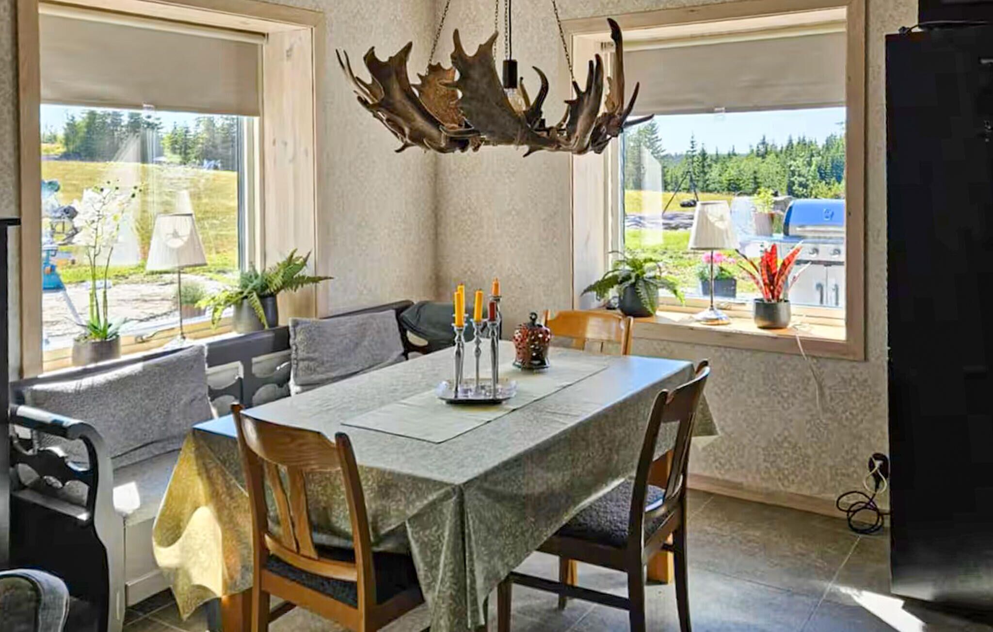 A dining area with a table set for four, a chandelier, and potted plants.