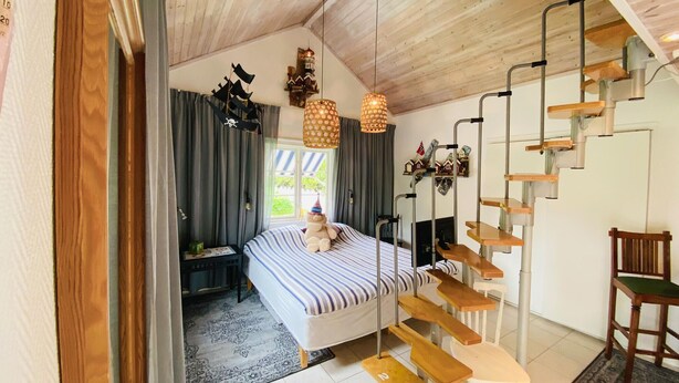 Une chambre à coucher avec un lit, une chaise, un bureau, un escalier et une fenêtre.
