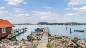 Une jetée en bois menant à un quai où sont amarrés des bateaux, un bâtiment rouge et une île lointaine.