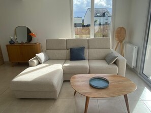 Un salon moderne avec un canapé d’angle beige, une table basse en bois et un buffet en bois.