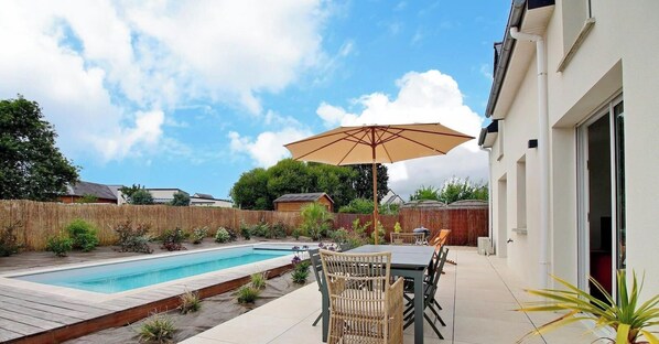 Un jardin avec une piscine, une table à manger entourée de chaises et un parasol.