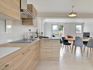 A modern kitchen with wooden cabinets, a central island, and a dining area with chairs and a table.