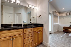 Une salle de bain avec des meubles en bois, un plan de toilette noir et un grand miroir avec éclairage intégré.