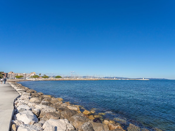 A coastal walkway with a rocky shoreline, a lighthouse, and a marina in the distance.