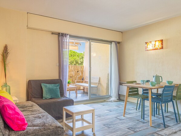 A cozy living area with a sofa, a small table, and a dining table with chairs. There is a sliding glass door leading to an outdoor patio.