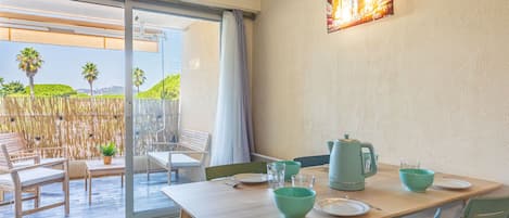 Uma área de refeições com uma mesa posta para dois, uma porta de vidro deslizante que dá para um pátio externo, e um luminário fixado na parede.