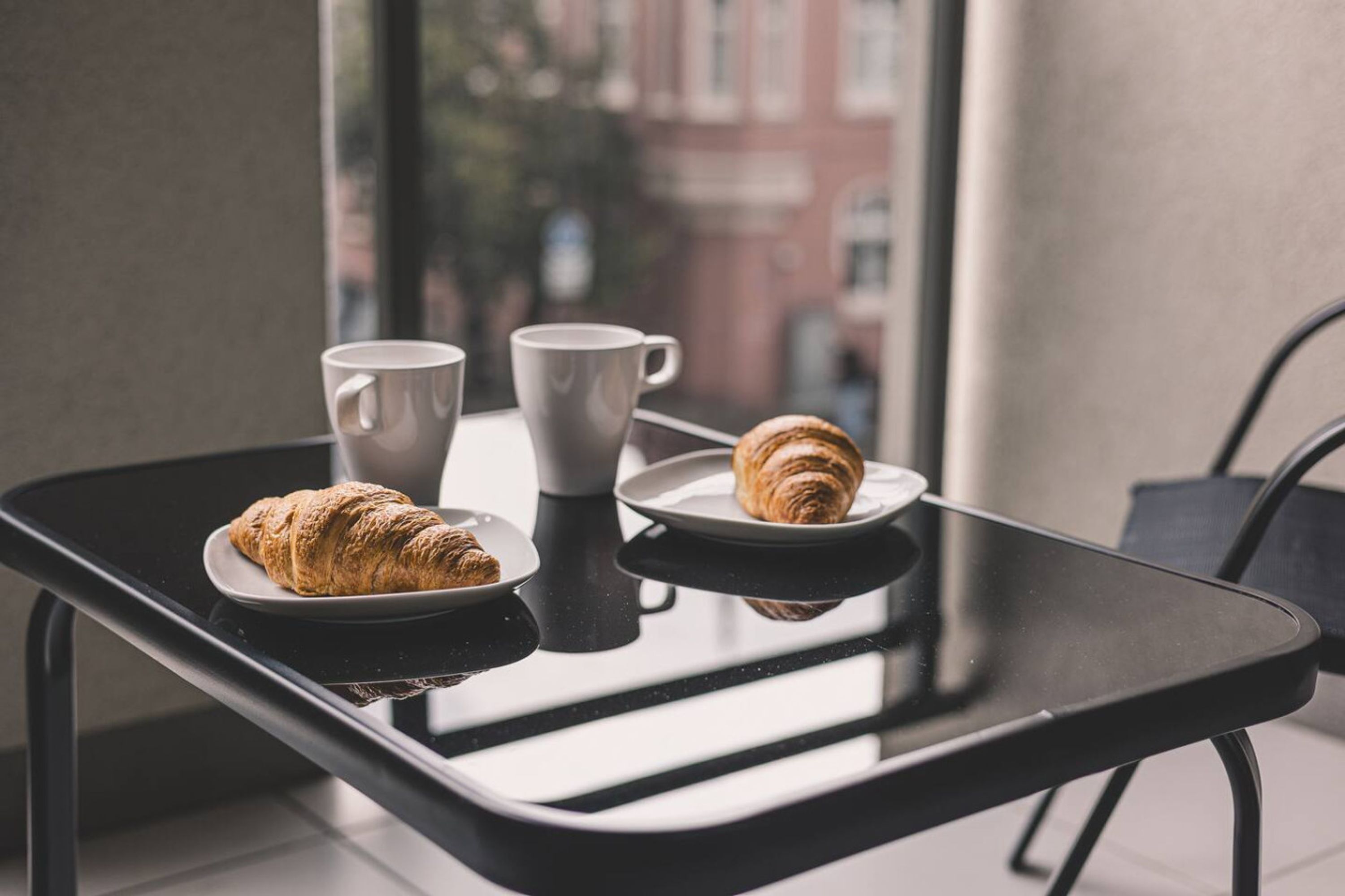 A table with a croissant, two white cups, and a plate with a croissant.