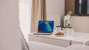 A modern living room with a laptop on a white table, a potted plant, a cup, and a plate with a pastry. - Blanco Apartament Gara Balkon (Bydgoszcz)